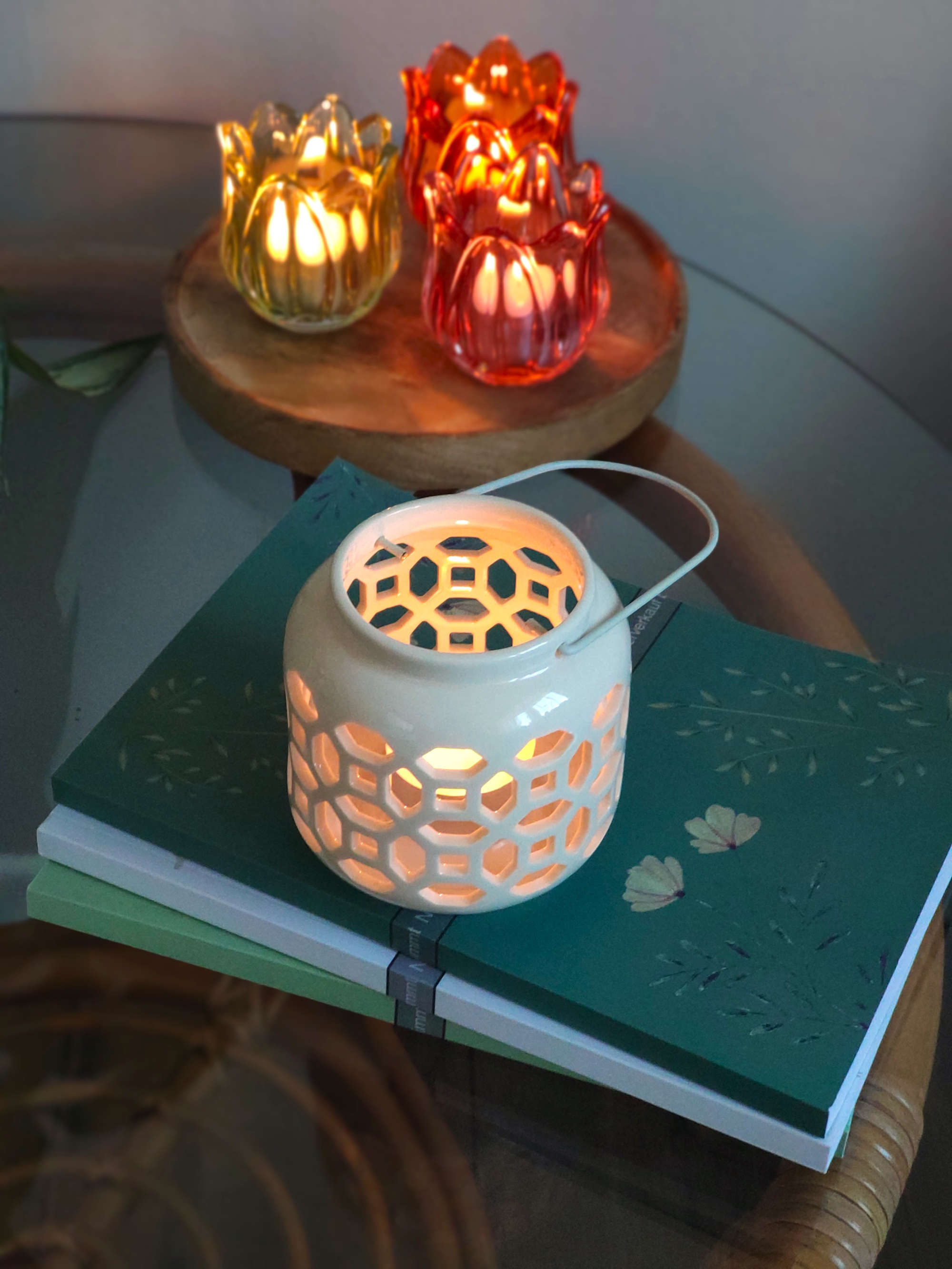 Windlicht aus Porzellan in Weiss mit Metallgriff auf einem Glastisch und Dekoration