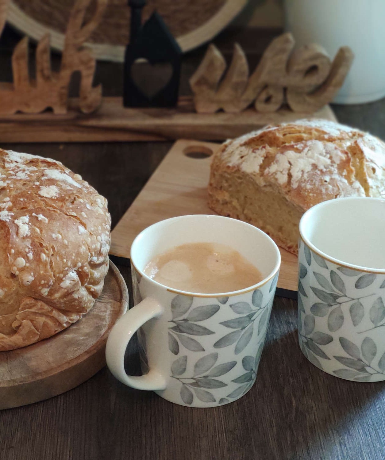 Tassen mit grauen Blätter Dekor und zwei Brote im Hintergrund